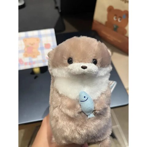 Blush beige otter plush keychain holding a blue fish